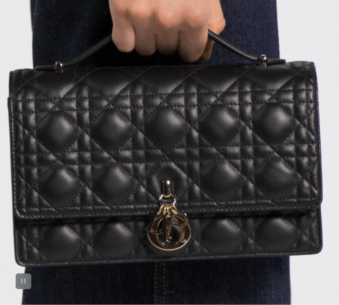 Black quilted leather crossbody bag with snap closure under the flap. There are charms attached to the front of the purse. This bag is available in 4 colors. It has a handle on top and a long strap.