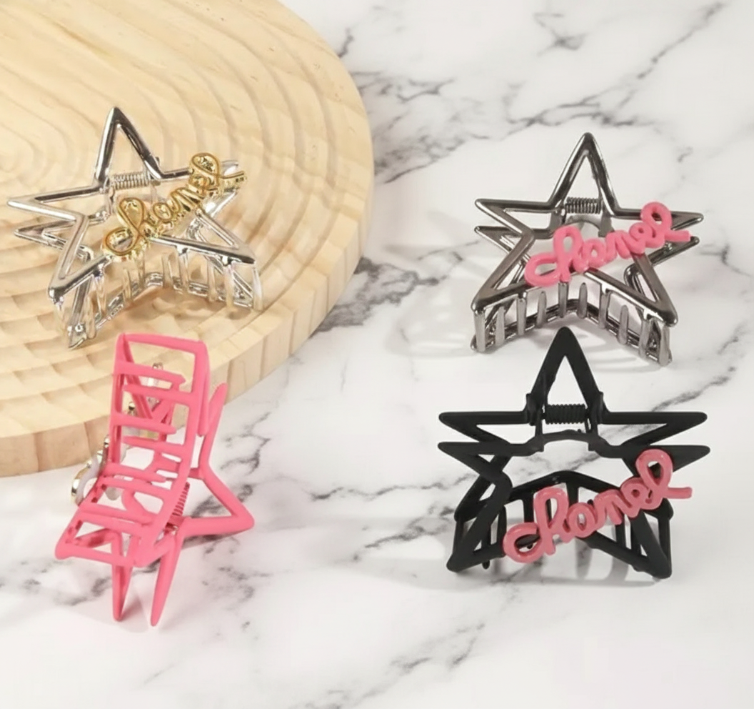medium sized, plastic, star-shaped hair clips, in four different color options, each has script lettered detail on the front.   The clips are on display with a White backdrop behind them.  