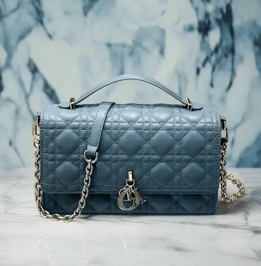 Shiny blue quilted leather CD crossbody handbag, with top handle. It has a silver chain strap & hardware, as well as silver charms on the front.  (Not MATTE) 