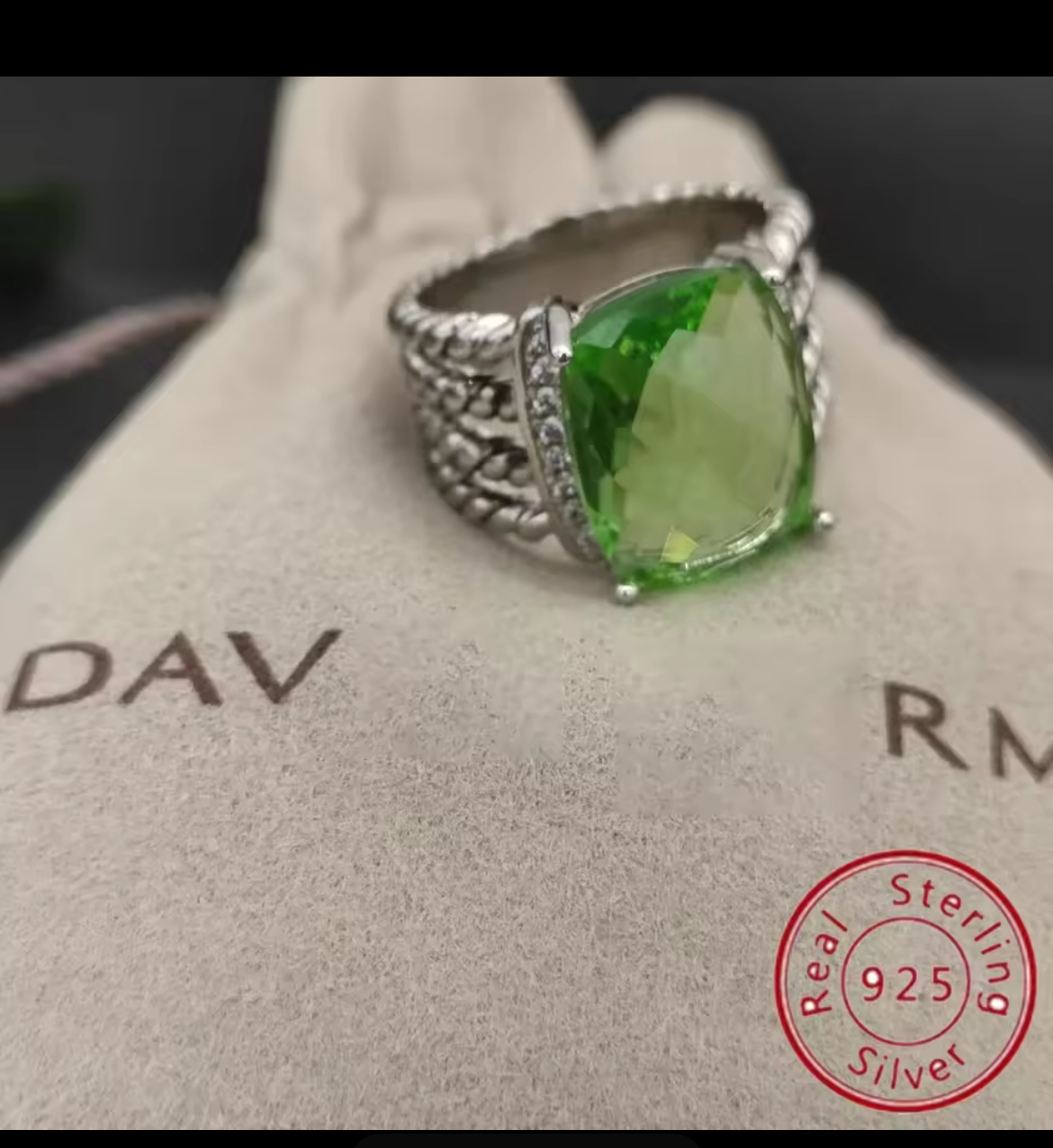 Green gemstone ring on a branded cushion with '925 Sterling Silver' stamp.