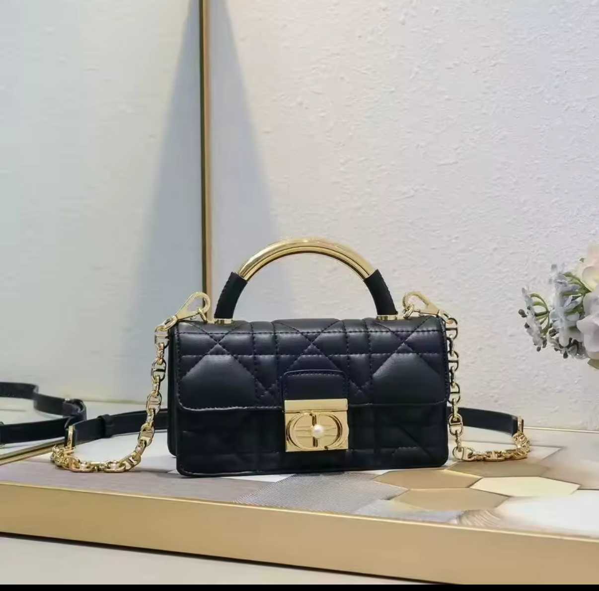 Black quilted handbag with gold accents on a light wooden surface.