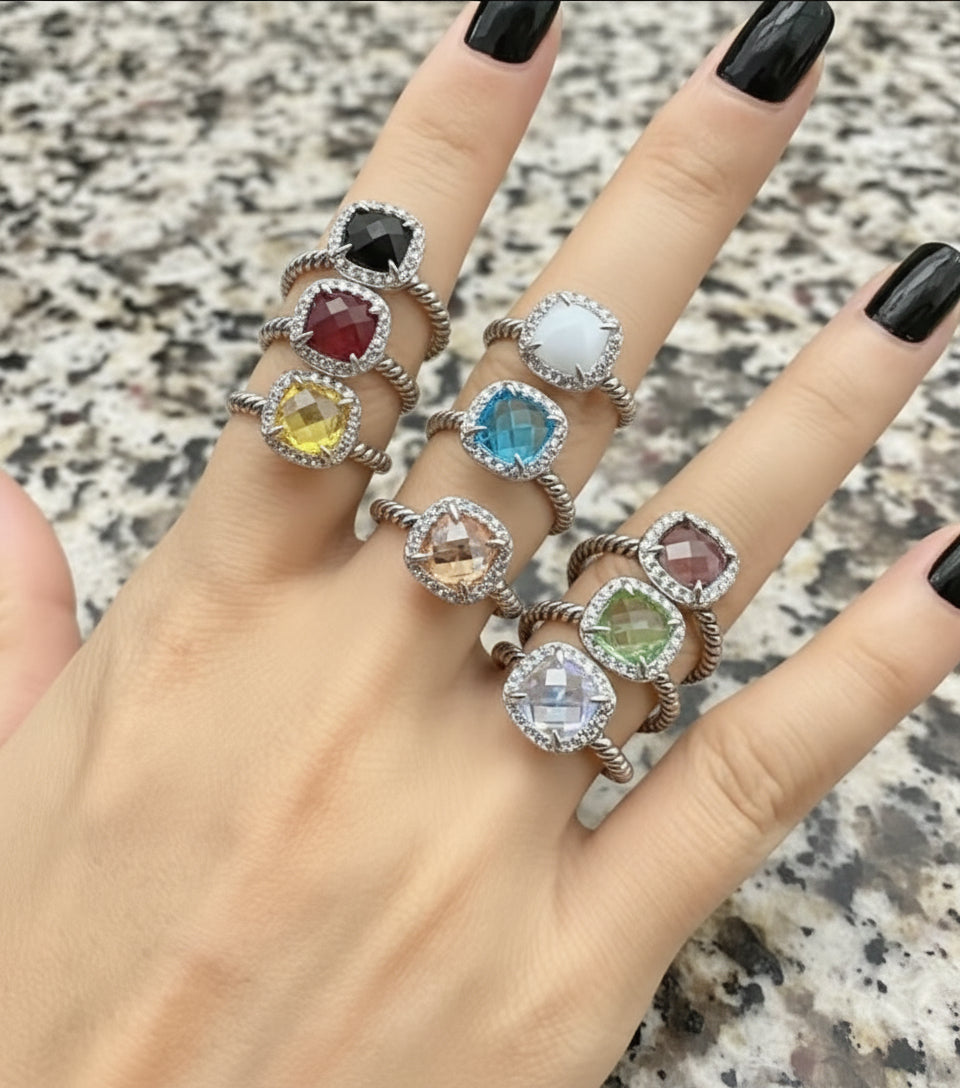 Hand wearing multiple rings with colorful gemstones on a dark background