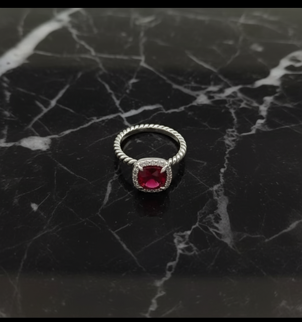 Silver ring with a red gemstone on a beige velvet bag