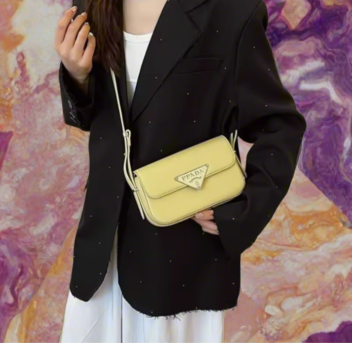 Person holding a yellow Prada handbag against a colorful abstract background
