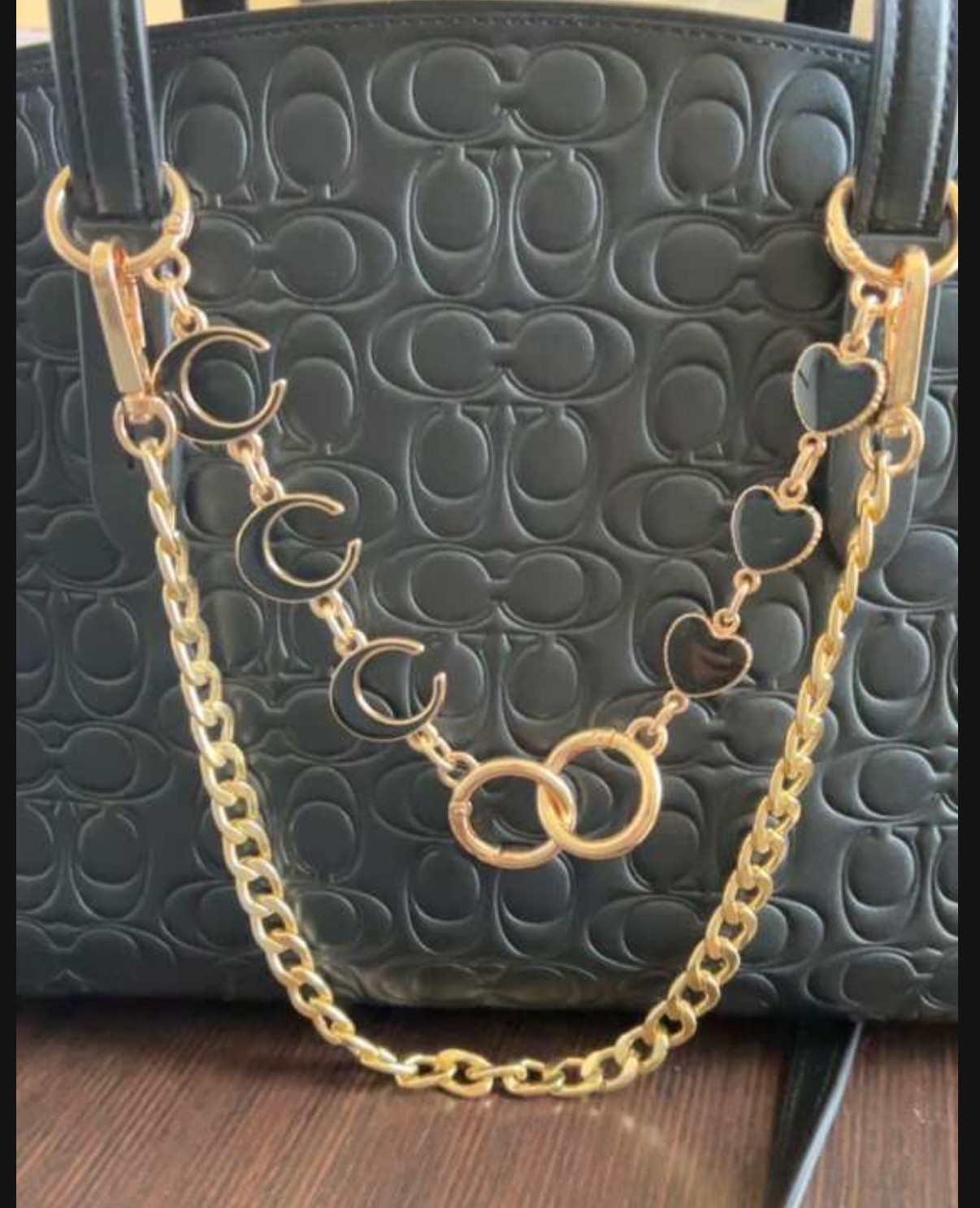 Gold chain necklace draped over a black textured handbag on a wooden surface.