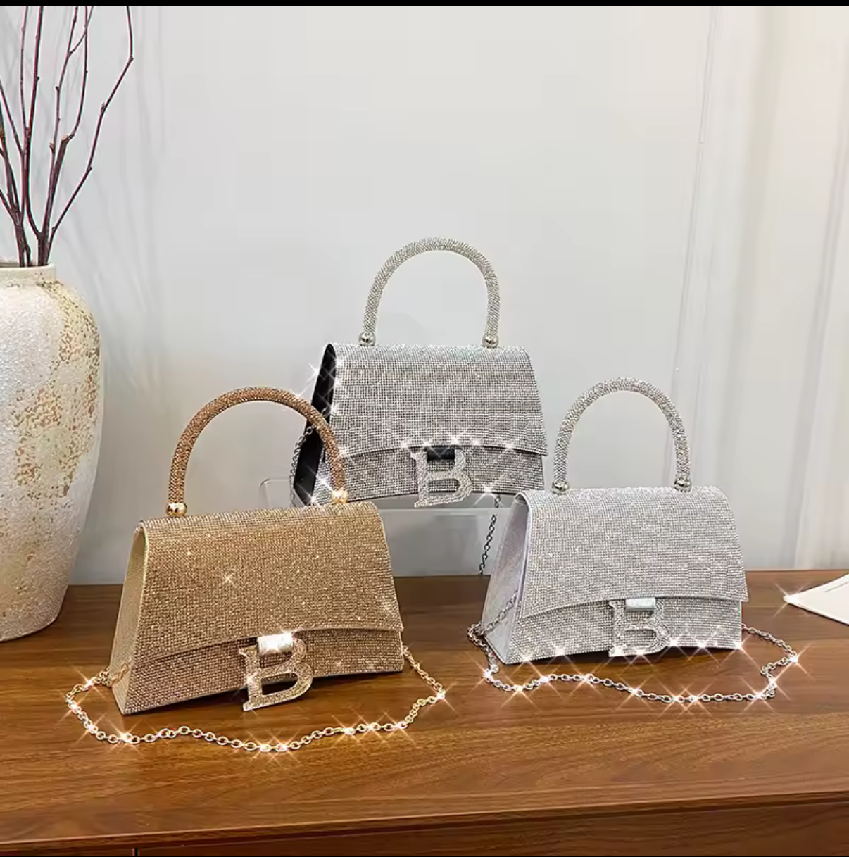Three crystallized clutch handbags with chain crossbody straps on a wooden surface with a neutral background